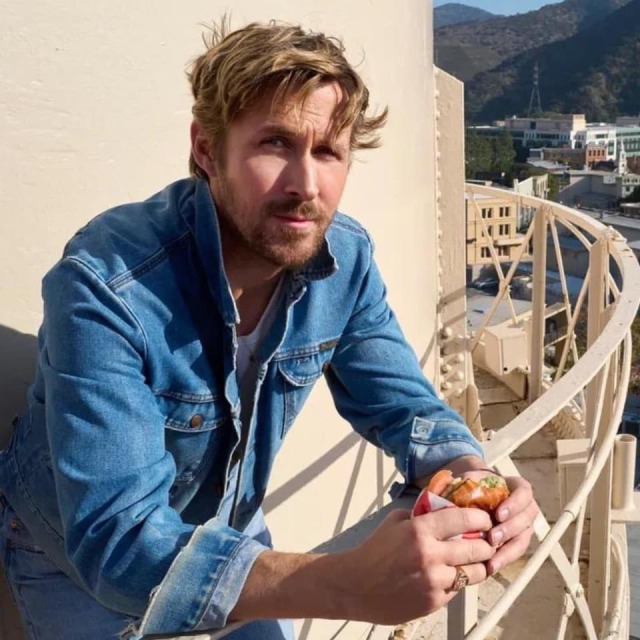 close up of Ryan Gosling on the WB water tower. he's wearing a jean jacket that matches the sky and nonchalantly leaning on the railing with an apple in his hands